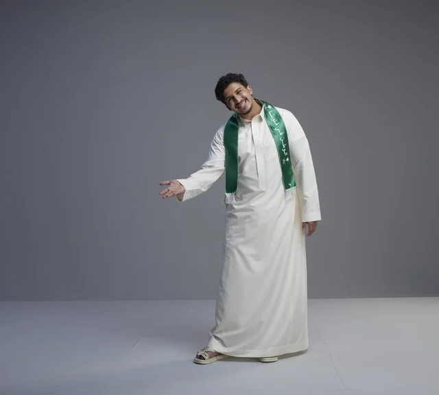 شاب سعودي يرتدي الثوب التقليدي والوشاح الوطني الأخضر