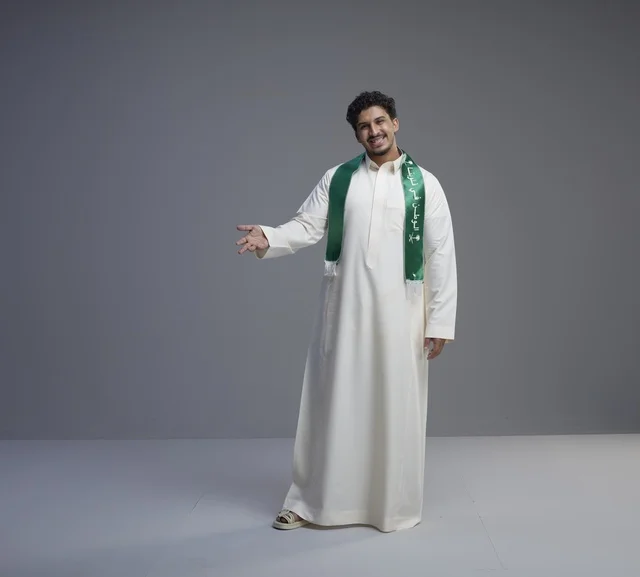 شاب سعودي بالوشاح الوطني يرحب أمام خلفية استوديو