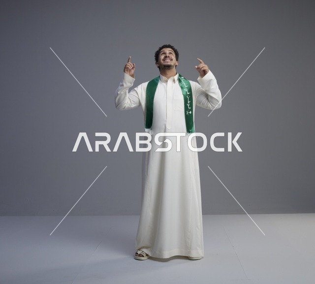 شاب سعودي بالثوب والوشاح الوطني يشير للأعلى