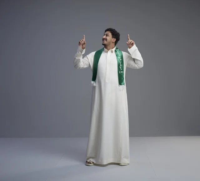 شاب سعودي بالوشاح الوطني يشير للأعلى