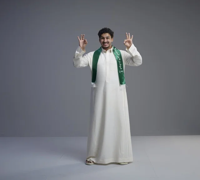 شاب سعودي بوشاح وطني وإشارة يد الموافقة