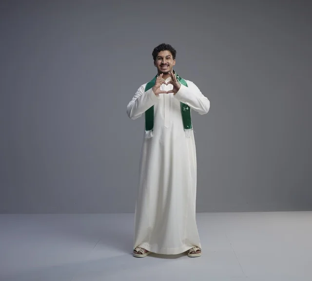 شاب سعودي يرتدي الوشاح الوطني الأخضر ويشكل رمز القلب