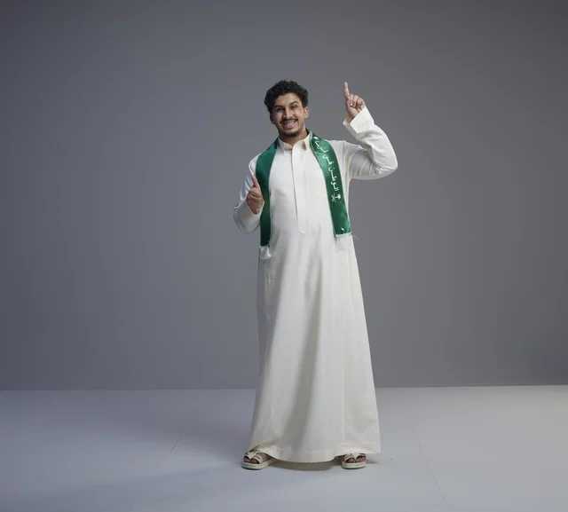 شاب سعودي بوشاح وطني يشير للأعلى