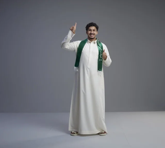 شاب سعودي بالوشاح الوطني يشير للأعلى