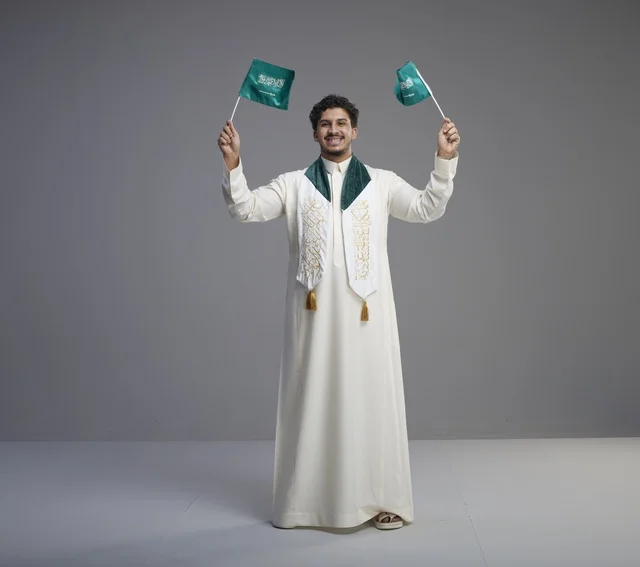 خريج سعودي مبتسم يحتفل ويحمل العلم الوطني في استوديو