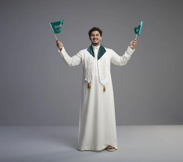 خريج سعودي بالثوب يحمل العلم الوطني في استوديو