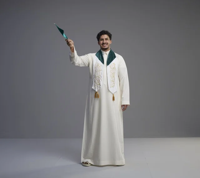 خريج سعودي يحمل العلم الوطني السعودي أمام خلفية رمادية