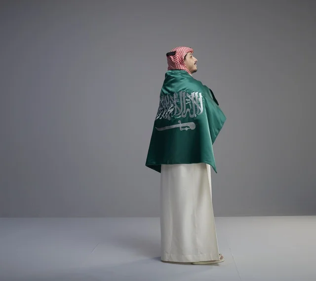 رجل سعودي يلتف بالعلم الوطني السعودي في الاستوديو