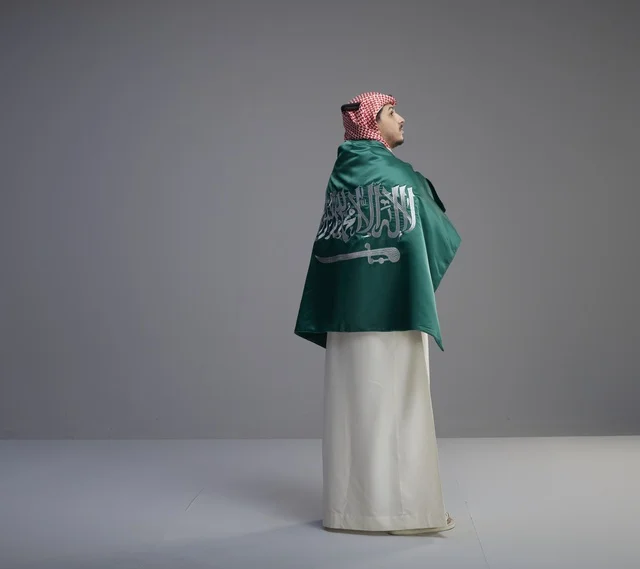 رجل سعودي بالعلم الوطني بالزي التقليدي