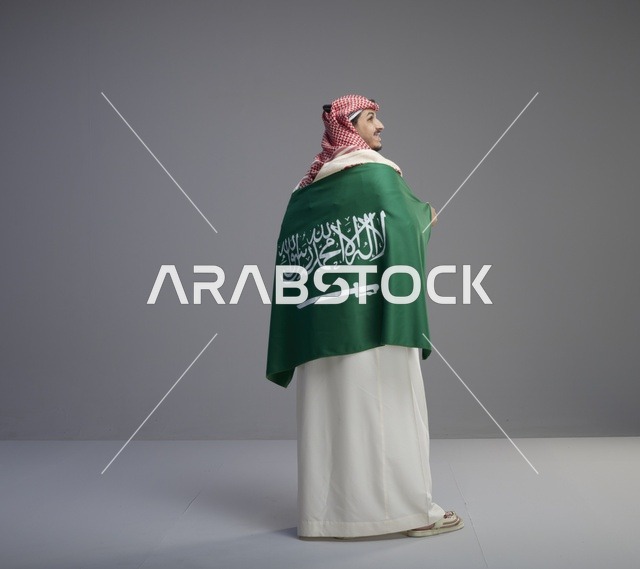 رجل سعودي يرتدي الثوب ويلتف بعلم السعودية