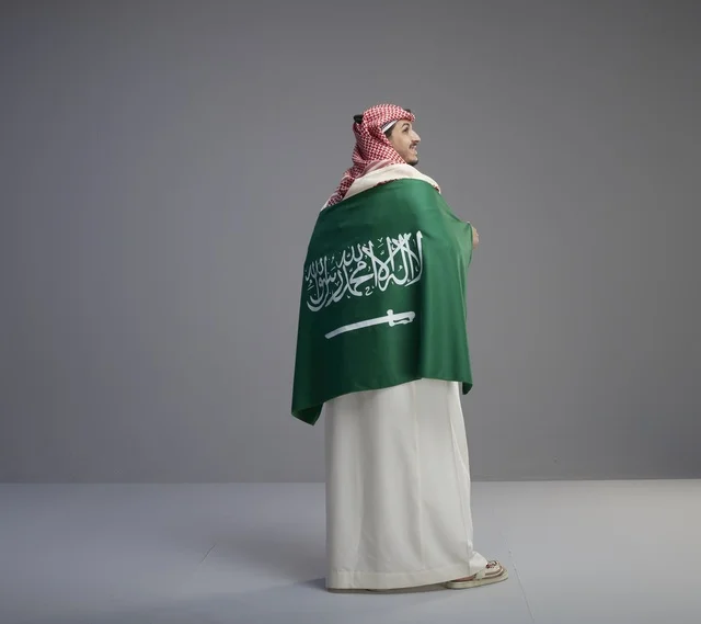 رجل سعودي يرتدي الثوب ويلتف بعلم السعودية