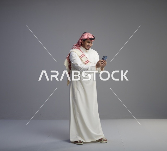 رجل سعودي بالثوب التقليدي يستخدم الهاتف الذكي