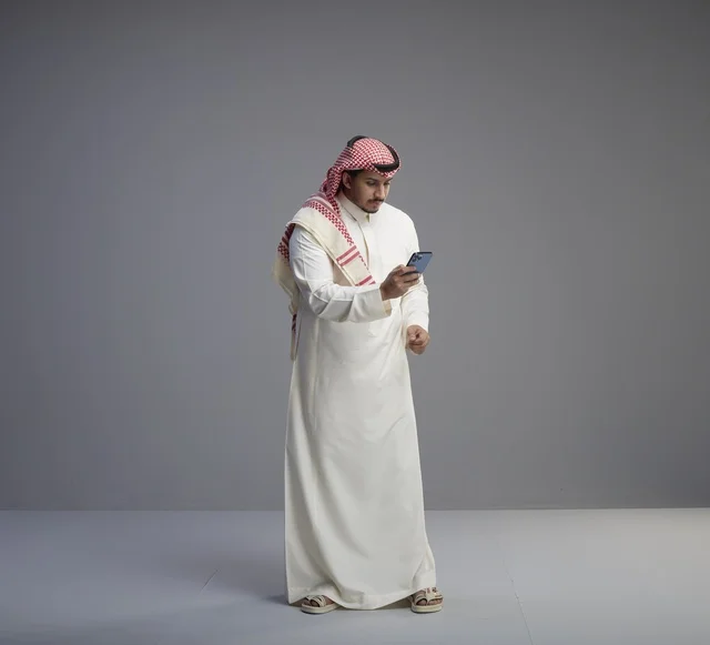 Saudi Man in Traditional Thobe Using Smartphone