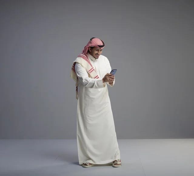 رجل سعودي يستخدم الهاتف الذكي على خلفية رمادية
