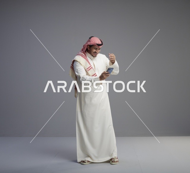 رجل سعودي بالثوب التقليدي يستخدم الهاتف الذكي في استوديو