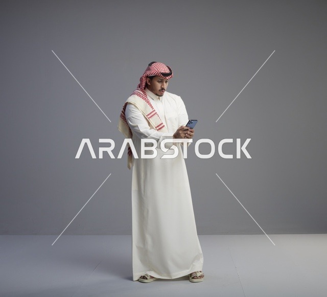 رجل سعودي بالزي التقليدي يستخدم الهاتف الذكي