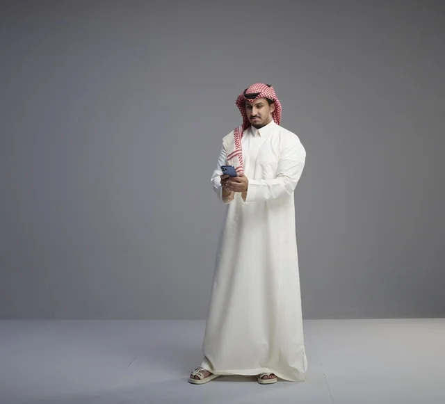 رجل سعودي يستخدم الهاتف الذكي بخلفية رمادية