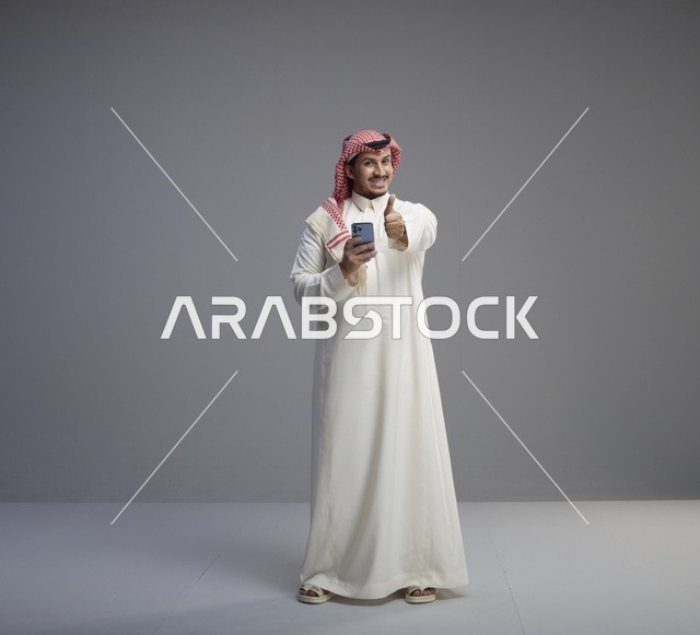 رجل سعودي مبتسم يستخدم الهاتف الذكي مع إيماءة الإبهام