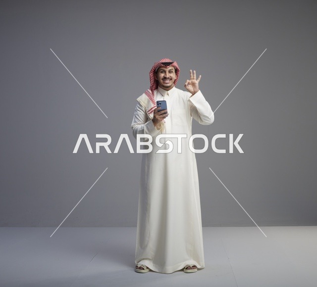 رجل سعودي مع هاتف ذكي يقوم بإشارة التمام