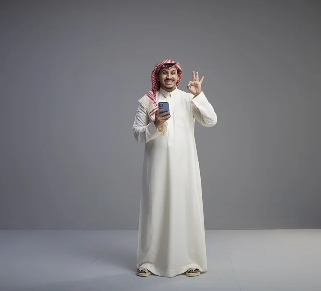 رجل سعودي مع هاتف ذكي يقوم بإشارة التمام