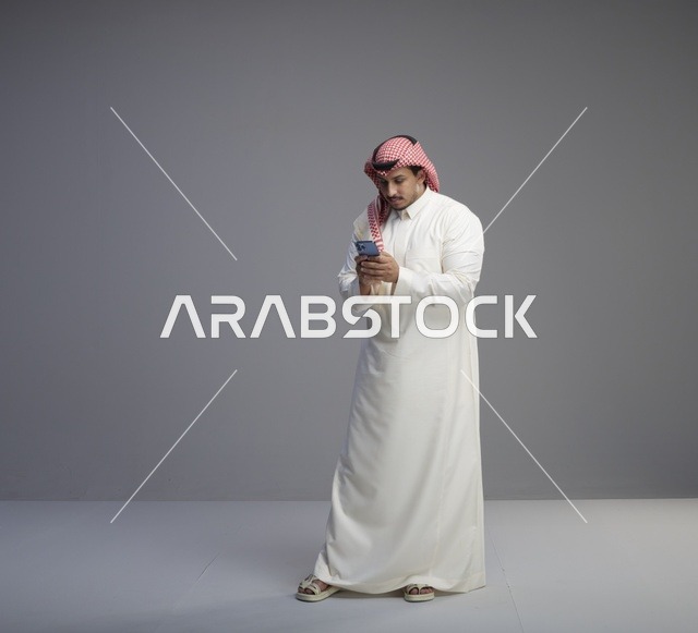 رجل سعودي بالثوب التقليدي يستخدم الهاتف الذكي في الاستوديو