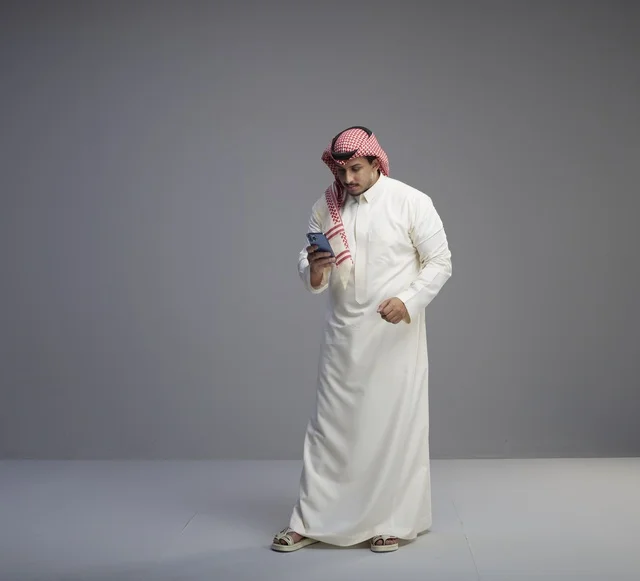 Saudi Man in Traditional Thobe Using Smartphone Studio