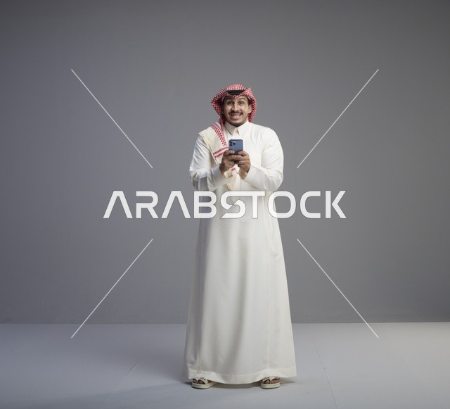 رجل سعودي يستخدم الهاتف الذكي في استوديو رمادي