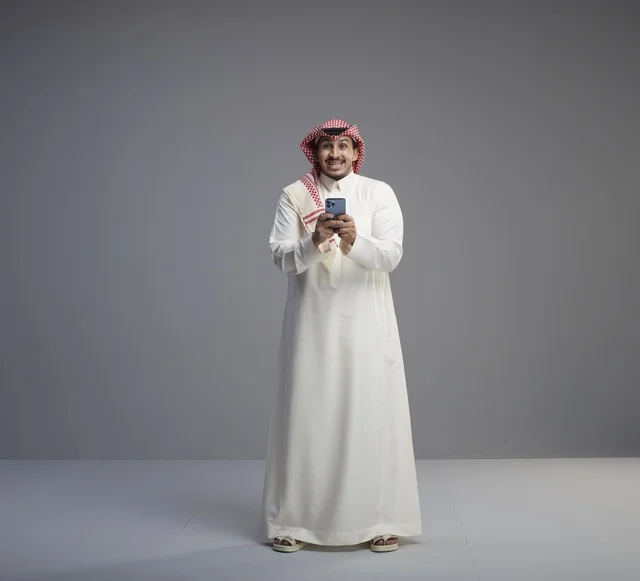 رجل سعودي يستخدم الهاتف الذكي في استوديو رمادي