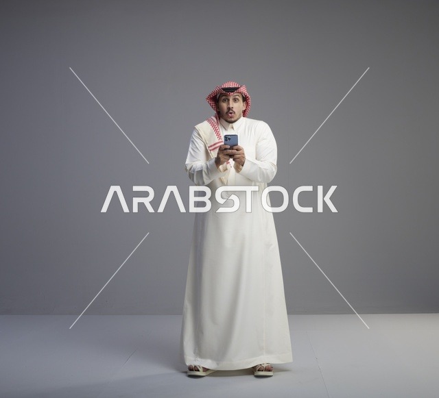 Surprised Saudi Man Using Smartphone on Grey Background