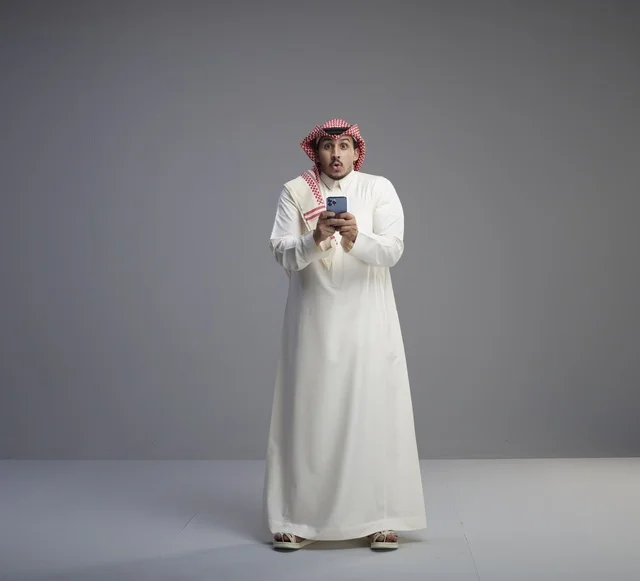 Surprised Saudi Man Using Smartphone on Grey Background