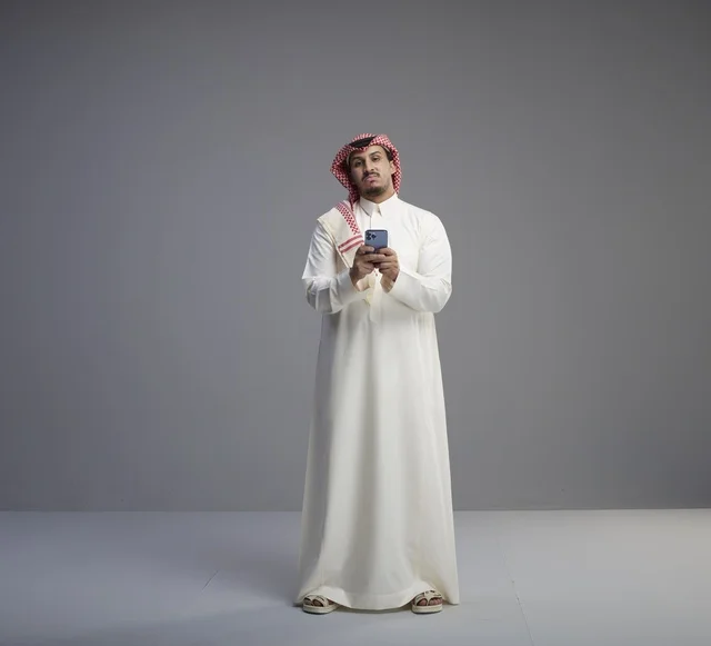 رجل سعودي بالثوب التقليدي يستخدم الهاتف الذكي
