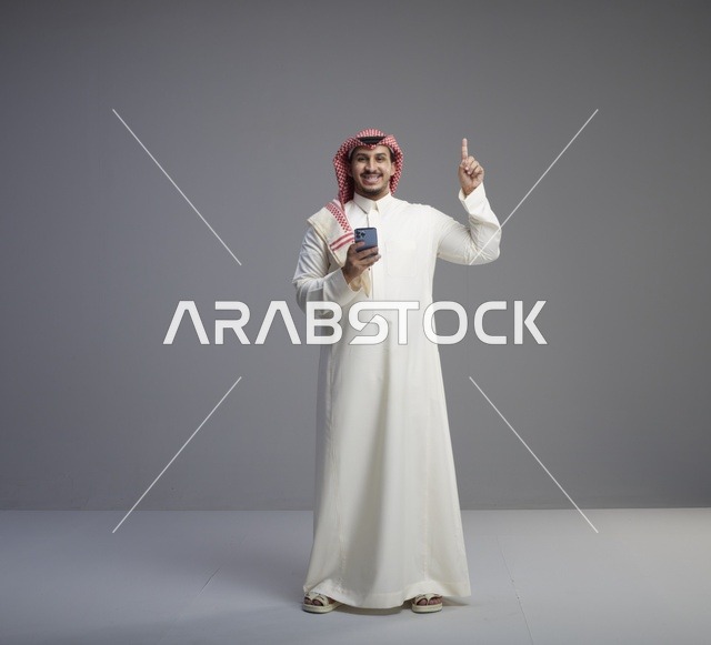 رجل سعودي يحمل جوال ويشير للأعلى في استوديو