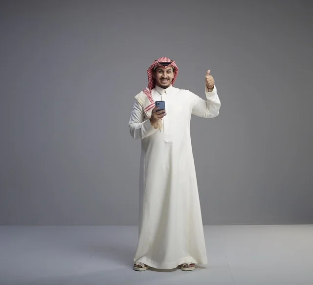 رجل سعودي يستخدم هاتف ذكي وإيماءة الإبهام