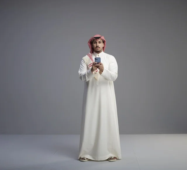 Saudi Man in Traditional Thobe Using Smartphone