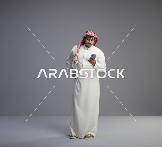رجل سعودي بالثوب التقليدي يستخدم الهاتف الذكي