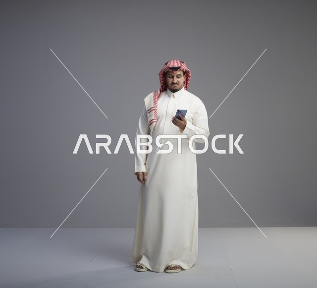 رجل سعودي يستخدم الهاتف الذكي بالزي التقليدي في الاستوديو