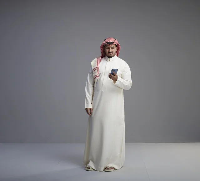 رجل سعودي يستخدم الهاتف الذكي بالزي التقليدي في الاستوديو
