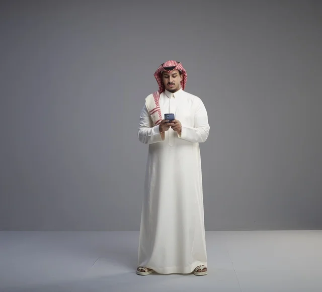 رجل سعودي بالثوب يستخدم الهاتف في الاستوديو