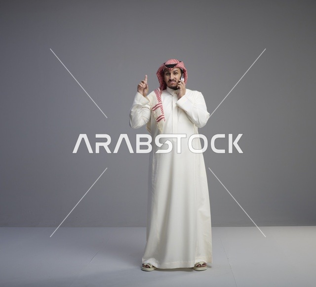 رجل سعودي يتحدث عبر الهاتف الذكي في استوديو رمادي
