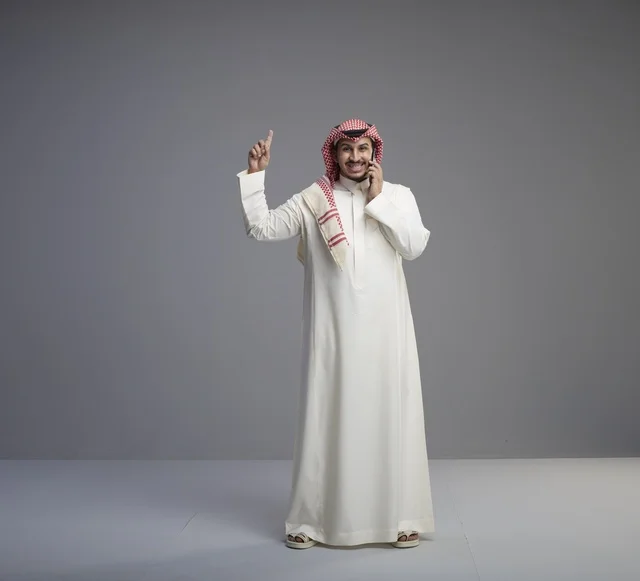 رجل سعودي بالزي التقليدي يتحدث عبر الهاتف الذكي ويشير للأعلى