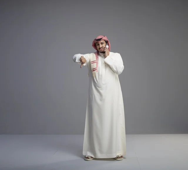 رجل سعودي يتحدث بالهاتف الذكي وينظر لساعة اليد