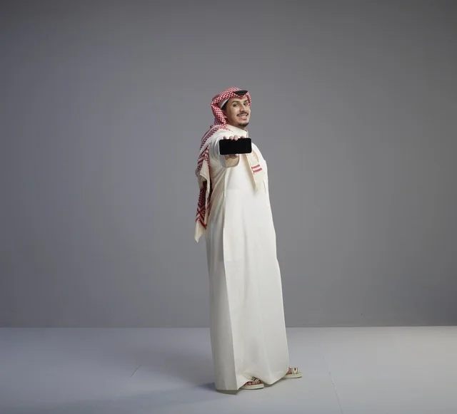 Saudi Man Holding Smartphone on Grey Studio Background