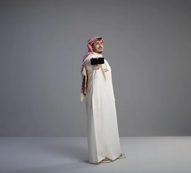 رجل سعودي يحمل نموذج هاتف ذكي في استوديو