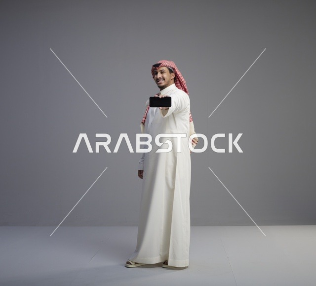 رجل سعودي يحمل نموذج هاتف ذكي بخلفية رمادية