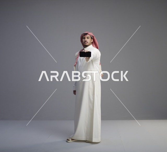 رجل سعودي يحمل هاتف ذكي بخلفية رمادية