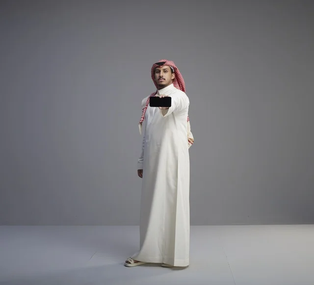 رجل سعودي يحمل هاتف ذكي بخلفية رمادية