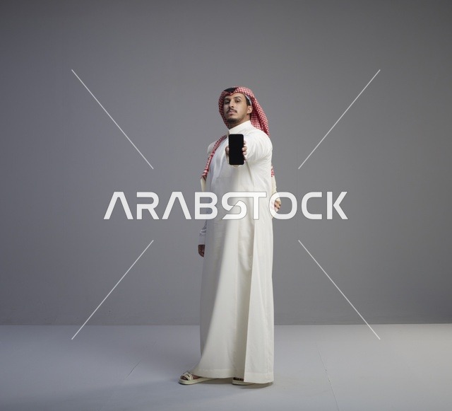 رجل سعودي يحمل هاتف ذكي في استوديو