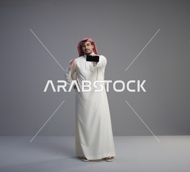 رجل سعودي يحمل هاتف ذكي بخلفية رمادية