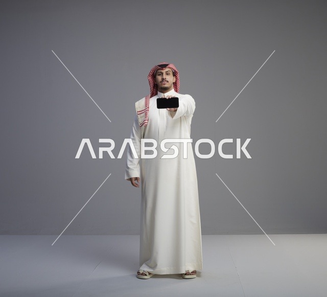 رجل سعودي يمسك هاتف ذكي في استوديو لقطة كاملة