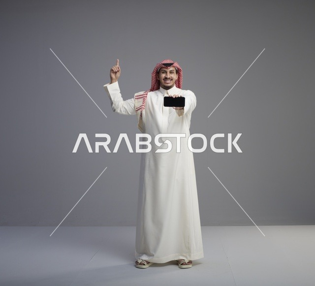 رجل سعودي يحمل هاتف ذكي ويشير للأعلى في استوديو